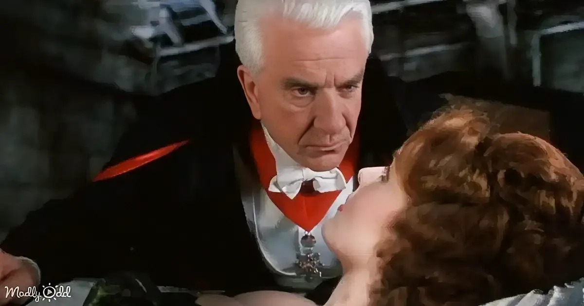 An older man in a black suit with red accents and a white bow tie is looking down at a woman with brown hair.