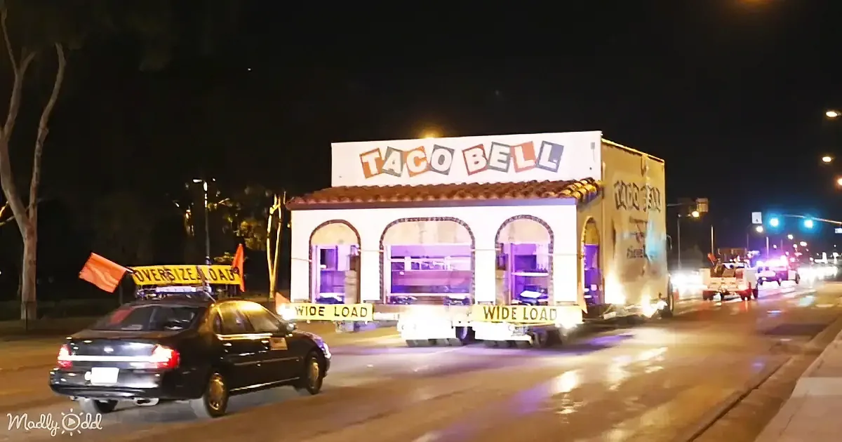A Taco Bell-themed truck is being transported on a wide load, with "OVERSIZE LOAD" and "WIDE LOAD" signs visible.