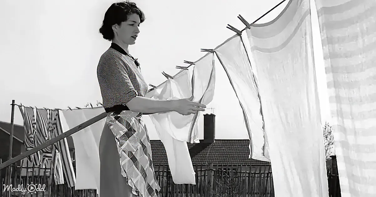 A woman hangs white laundry on a clothesline in a suburban setting.