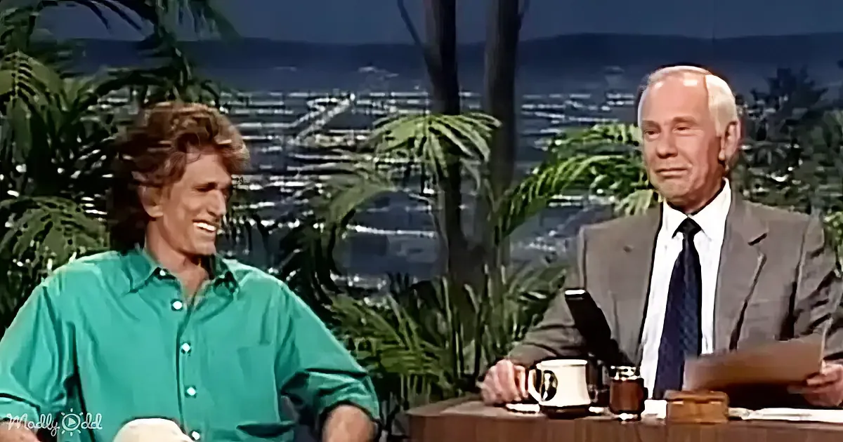 Michael Douglas in a green shirt smiles on a talk show set with a man in a suit.