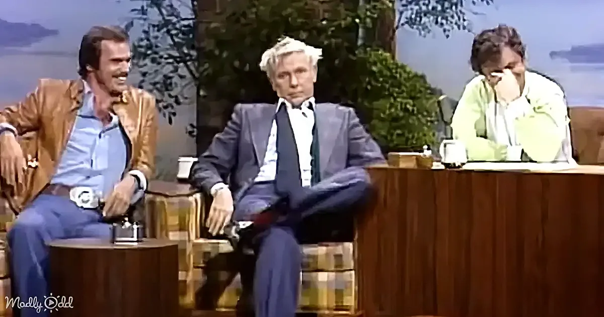 Three individuals seated on a talk show set with a backdrop of trees and water.