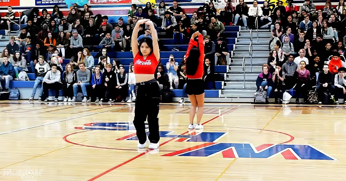 Two dancers in red and black perform on a basketball court with a crowd watching.