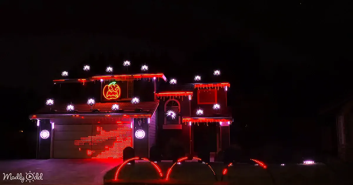 A house adorned with Halloween-themed lights, including a glowing pumpkin and ghostly figures, stands illuminated against...