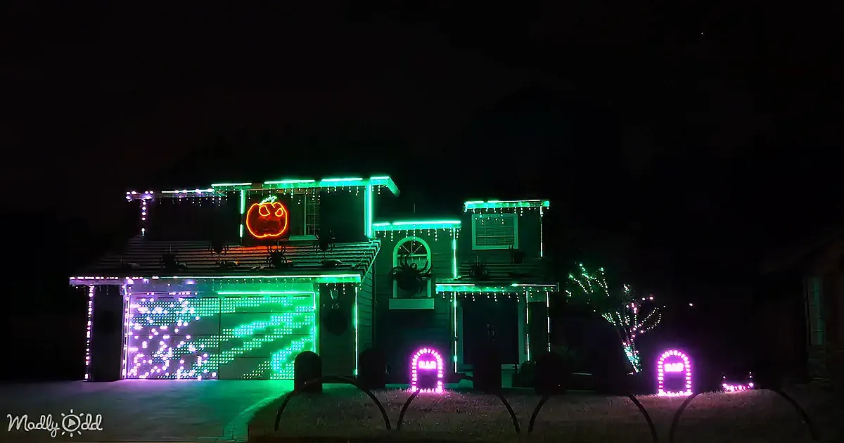 A house is decorated with Halloween lights, featuring a glowing pumpkin and spider decorations.
