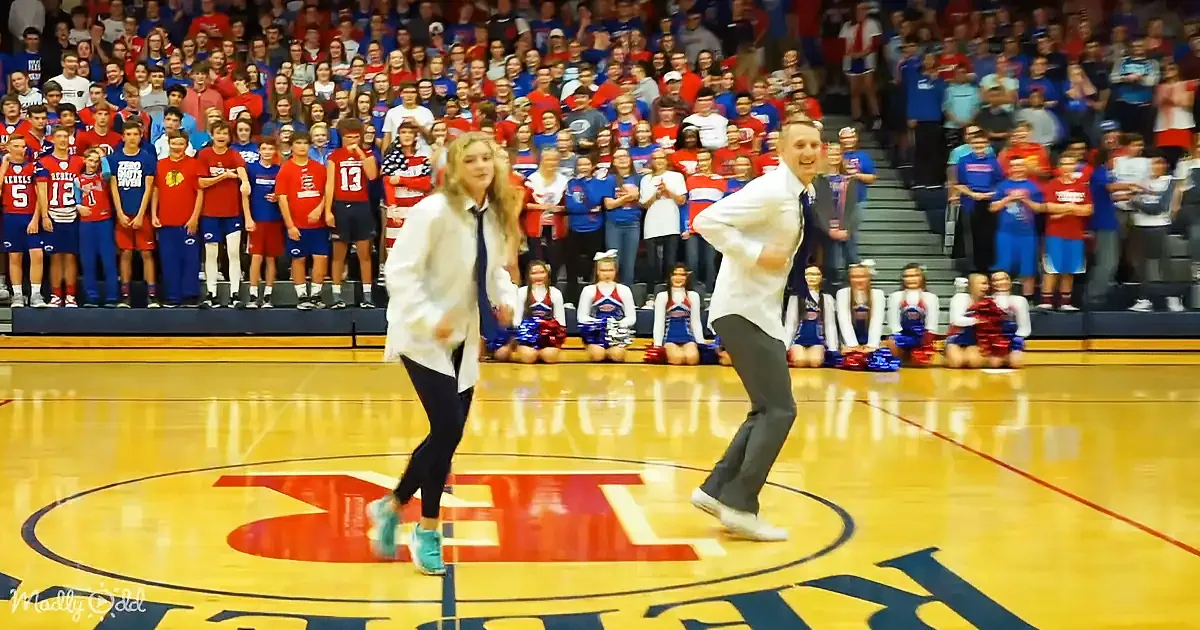 A man and woman dance on a basketball court in front of a cheering crowd and cheerleaders.