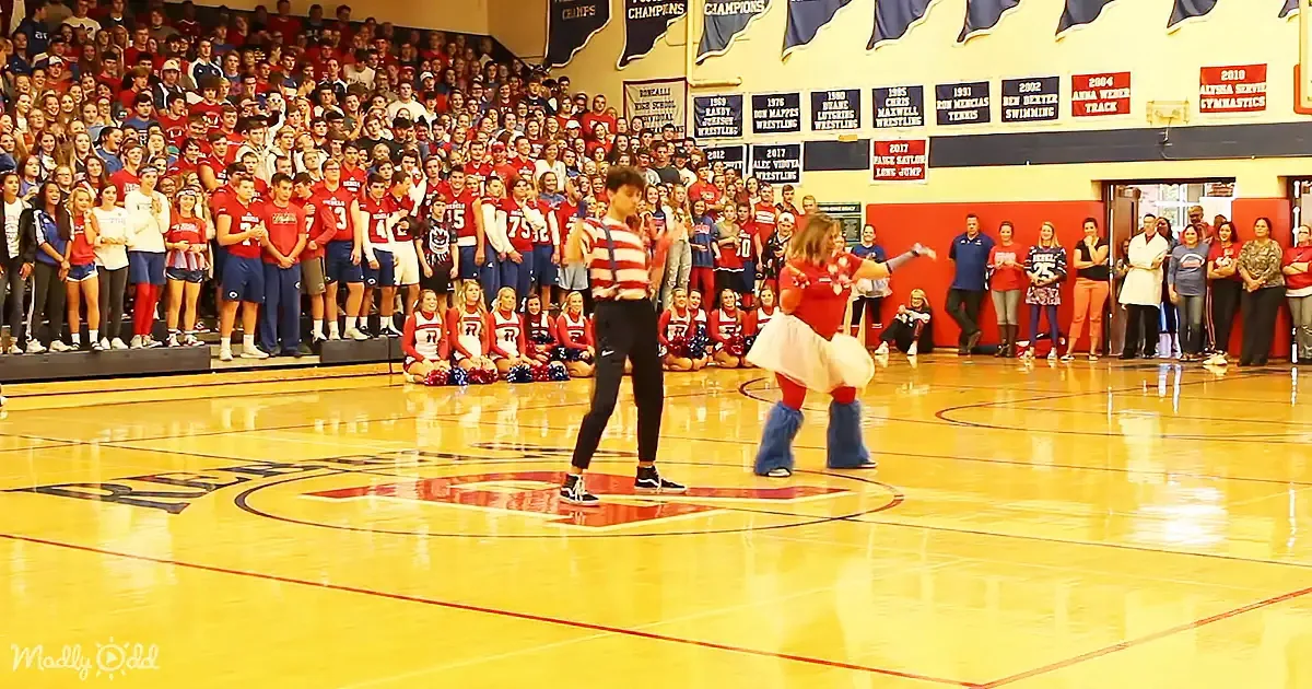 Two dancers perform on a basketball court in front of a large audience in a gymnasium.