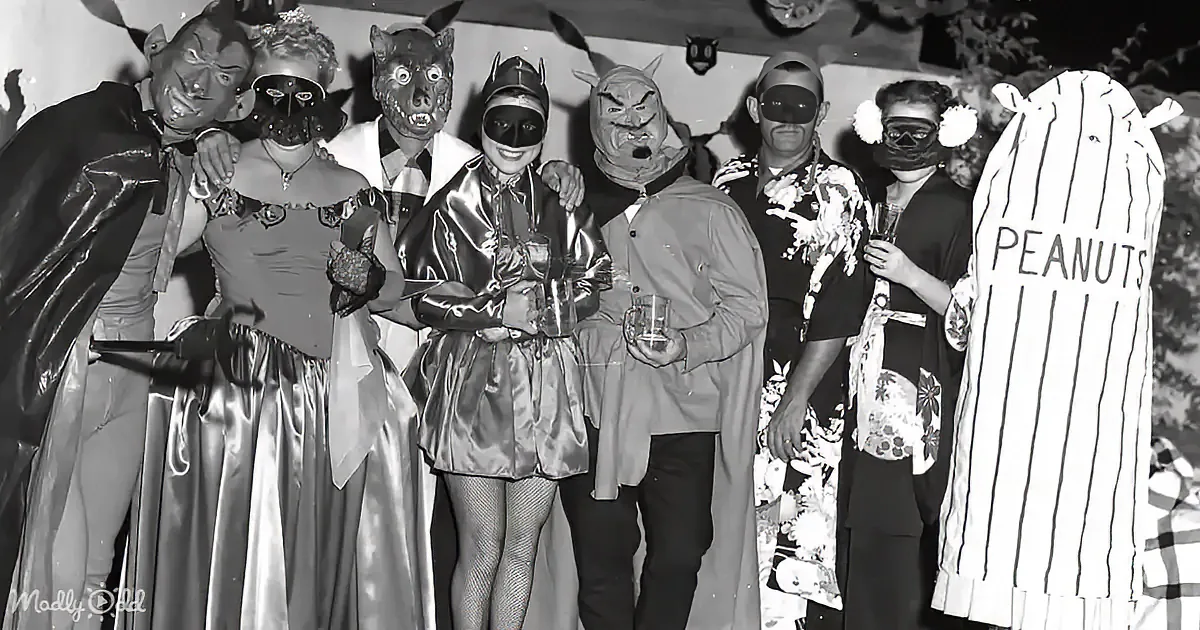 A group of people in various costumes, including masks and animal heads, stand together at what appears to be a themed...