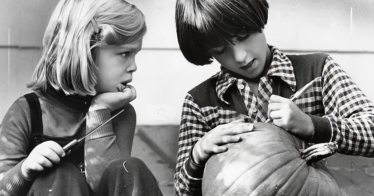 Two children with painted faces hold carved pumpkins, dressed in costumes, against a dark background.