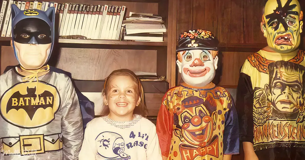 A child in a Batman costume stands next to a girl and two other children in clown and Frankenstein costumes.