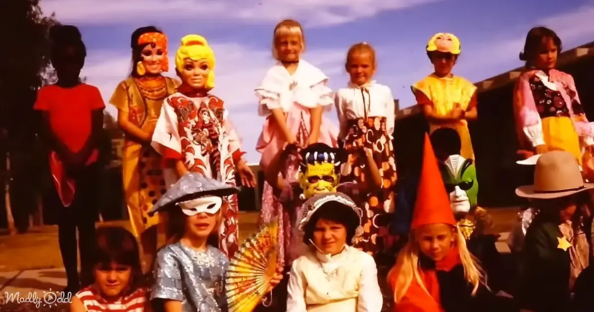 Children in various costumes, including a Frankenstein and a witch, pose for a group photo outdoors.