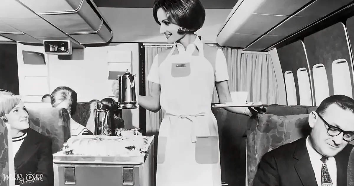 A flight attendant in a white uniform serves drinks to passengers in a vintage airplane cabin.