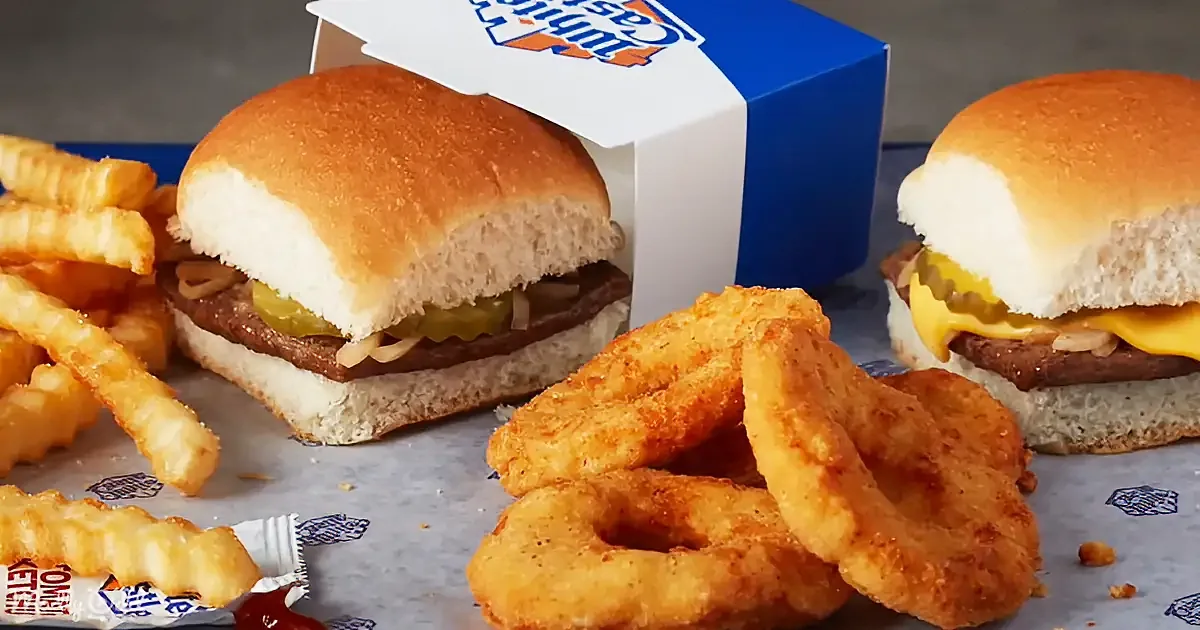 Two burgers with cheese and pickles, fries, and onion rings on branded paper.