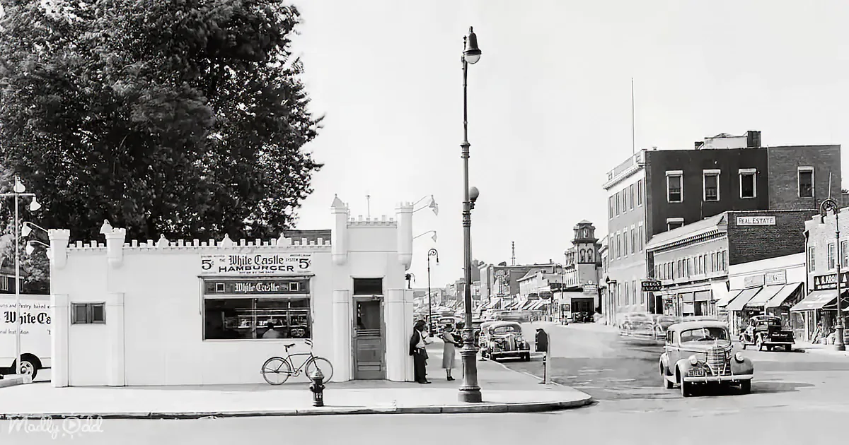 A vintage White Castle hamburger stand with people and cars on a busy street corner.
