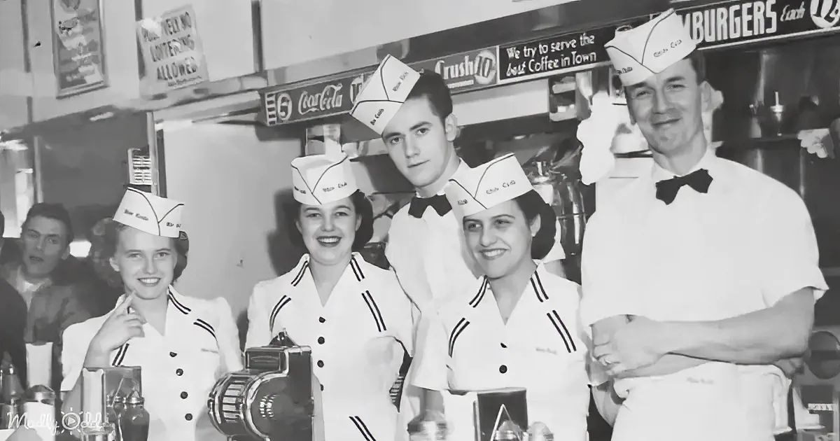 Waiters and waitresses in white uniforms with hats pose in a diner setting.