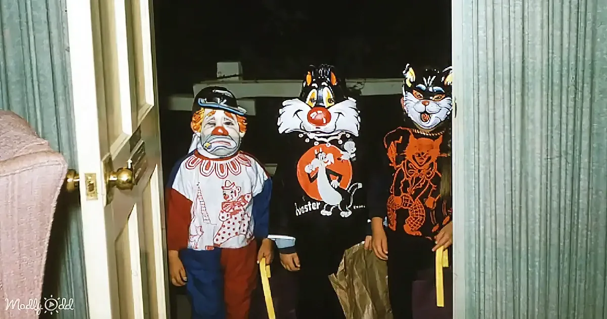 Three children in costumes, including a clown and two cats, stand in a doorway.