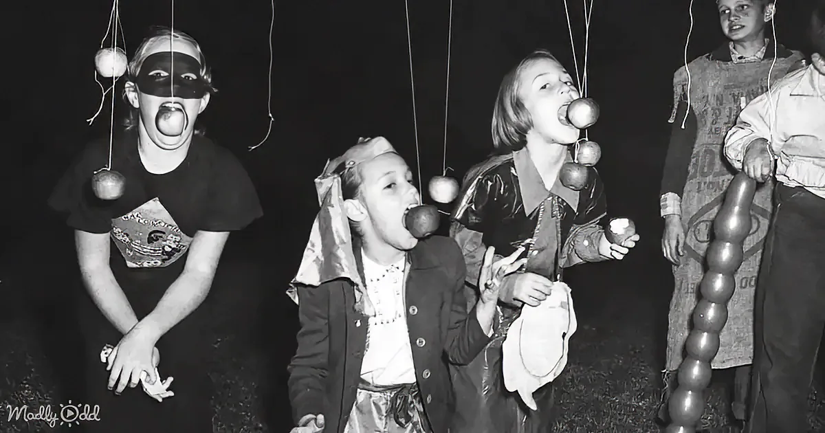 Two children in costumes, one in a mask and the other in a dress, smile and hold small items.