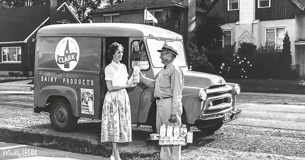 A dairy delivery man in uniform hands a product to a woman in a dress near a vintage Clark Dairy Products truck.