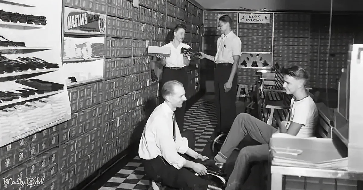A man hands a box to a woman in a store aisle, while another man and woman sit nearby.