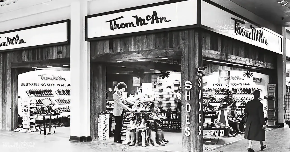 Thom McAn shoe store with wooden facade, displays various footwear, and customers browsing inside.