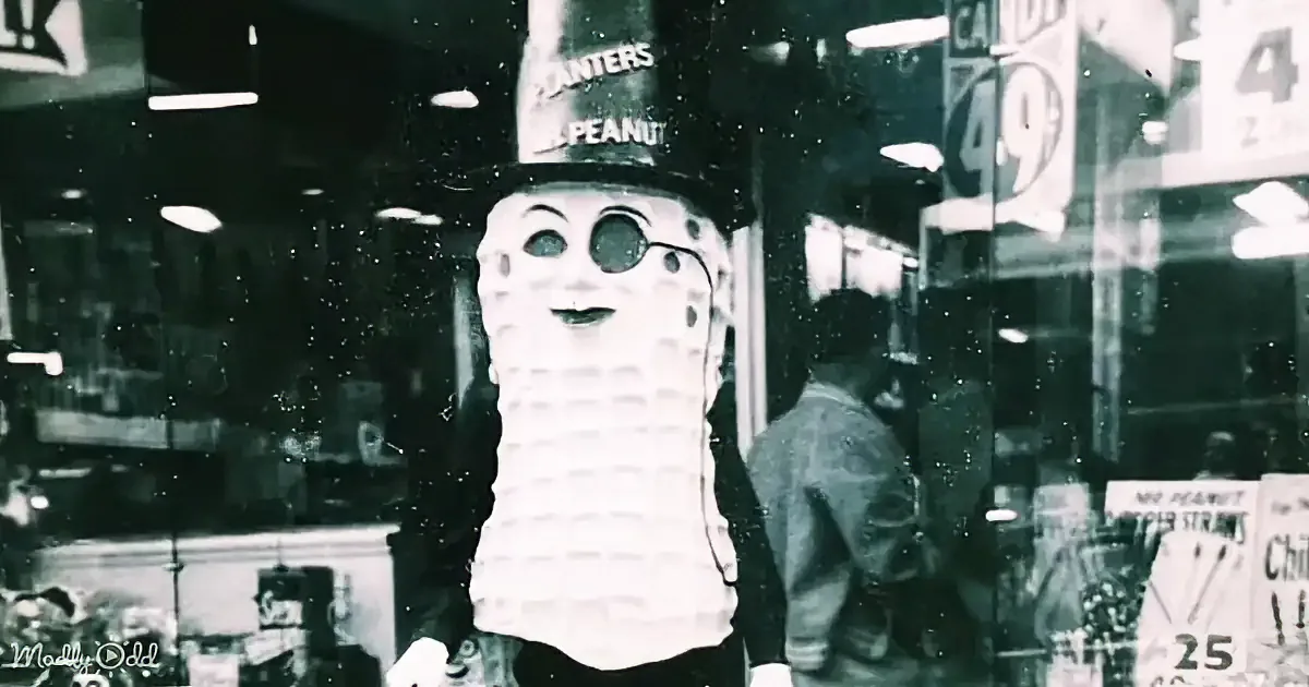 A person in a Mr. Peanut costume stands in front of a store window, wearing a hat and a mask.