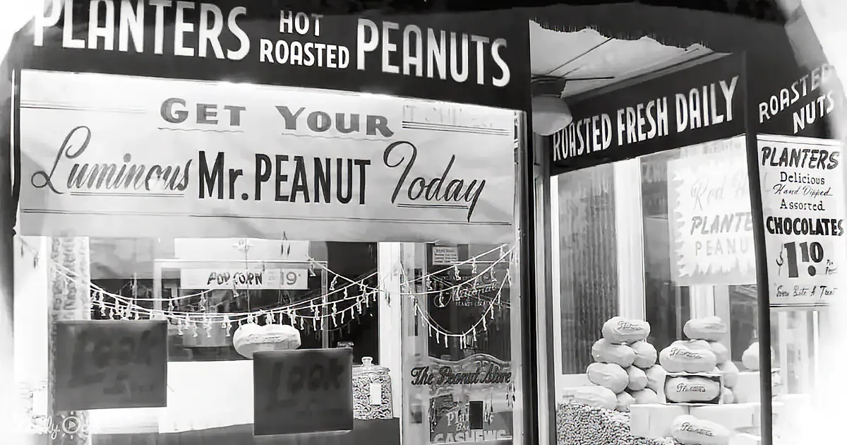 A vintage storefront displays Planters Hot Roasted Peanuts, with signs advertising fresh daily roasting and a glowing Mr...