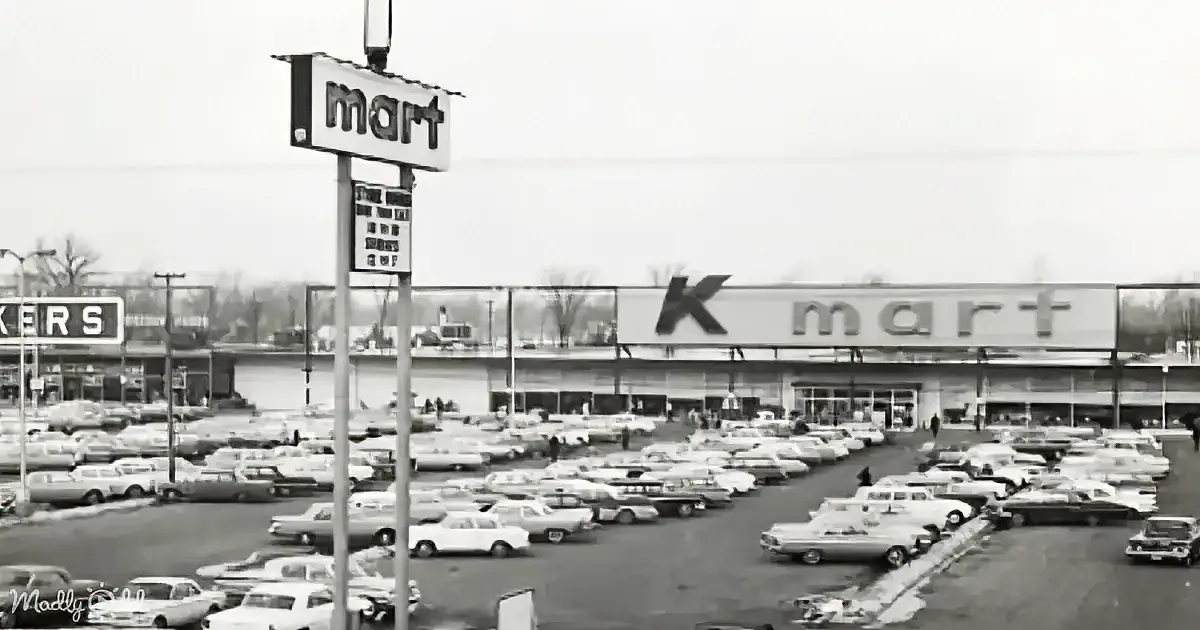 A bustling Kmart parking lot filled with vintage cars, signifying a busy shopping day.
