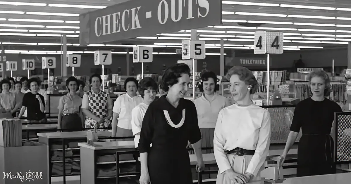 Two women in a bustling 1950s-era grocery store, surrounded by checkout counters and smiling.