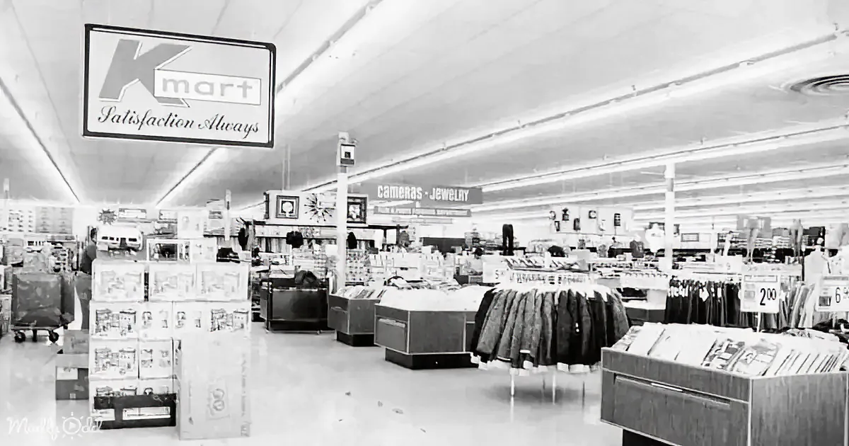 A vintage Kmart store interior with "Satisfaction Always" sign, neatly arranged products, and a clock on the wall.