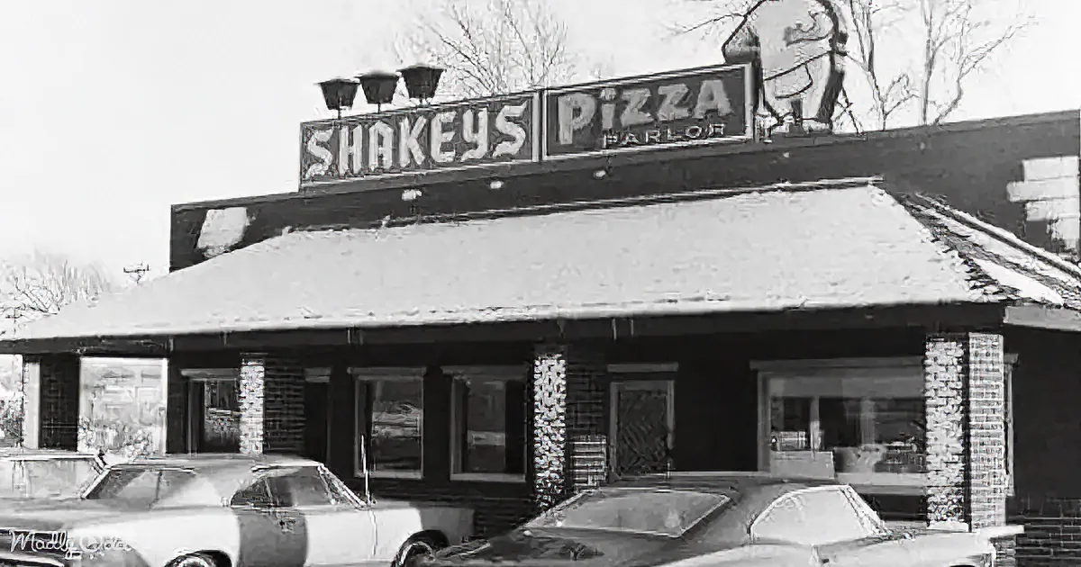 Shakey's Pizza Parlor sign atop a brick building with parked cars in front.