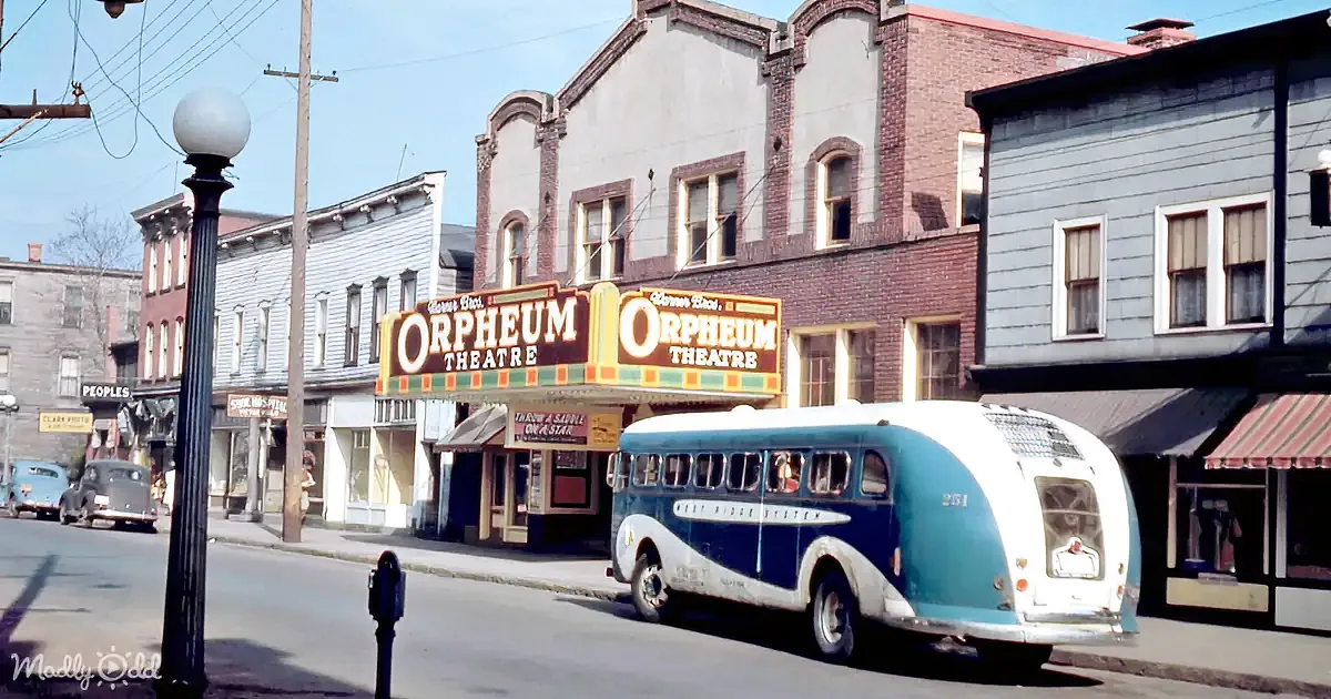 A vintage bus with a blue and white design is parked in front of the Orpheum Theatre on a sunny day.