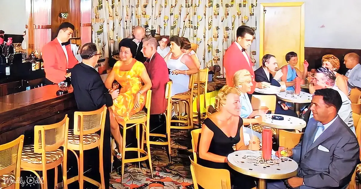 A group of people in a bar and restaurant setting, dressed in formal attire, interacting and enjoying drinks and food.