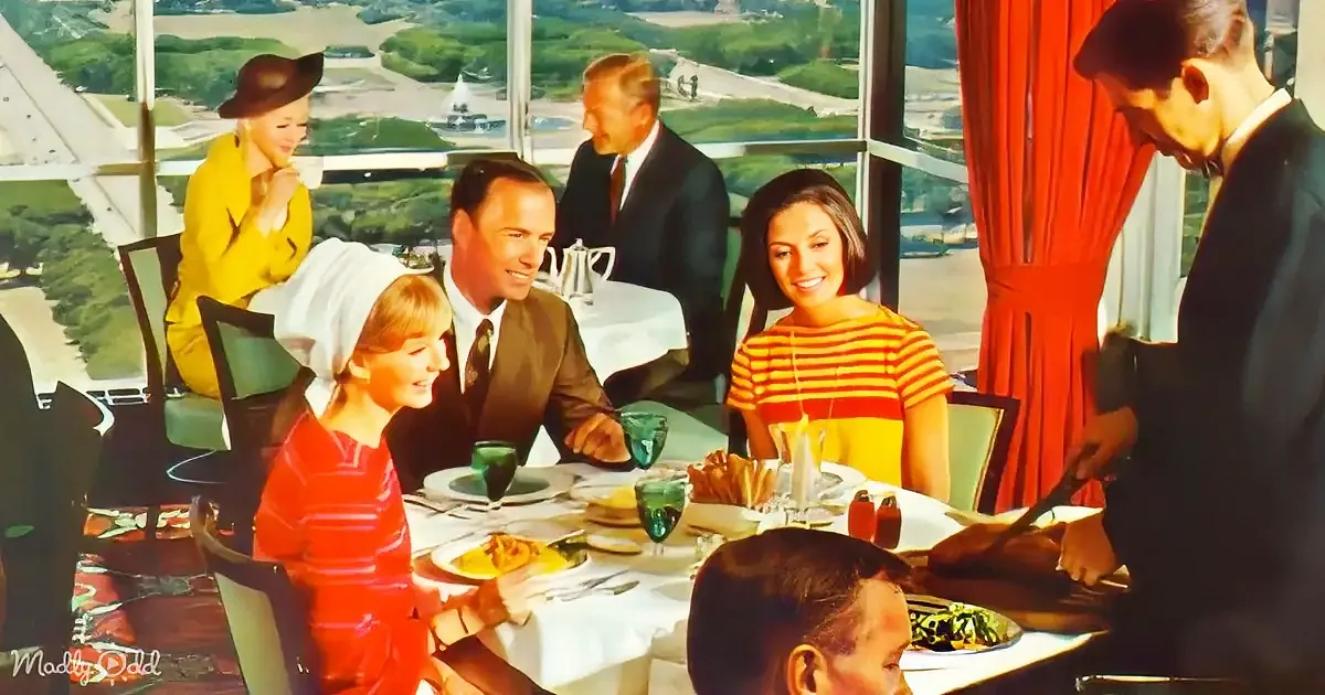 A waiter slices meat at a table with a family enjoying a meal in a restaurant with a scenic view.