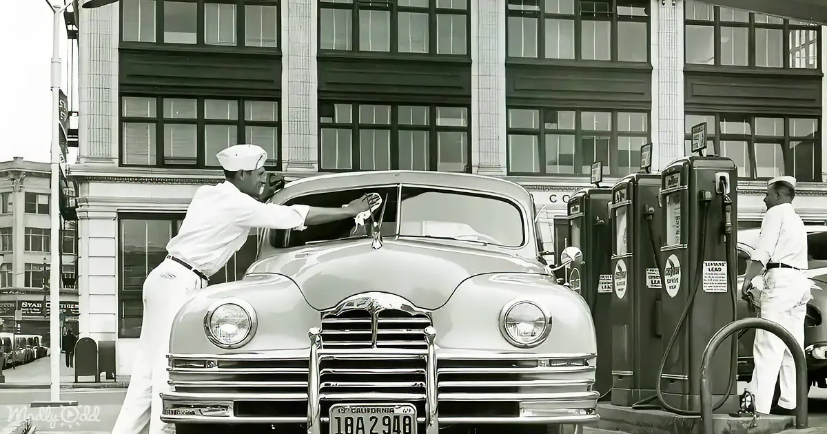 A man in a white uniform fills a classic car with gas at a vintage gas station.