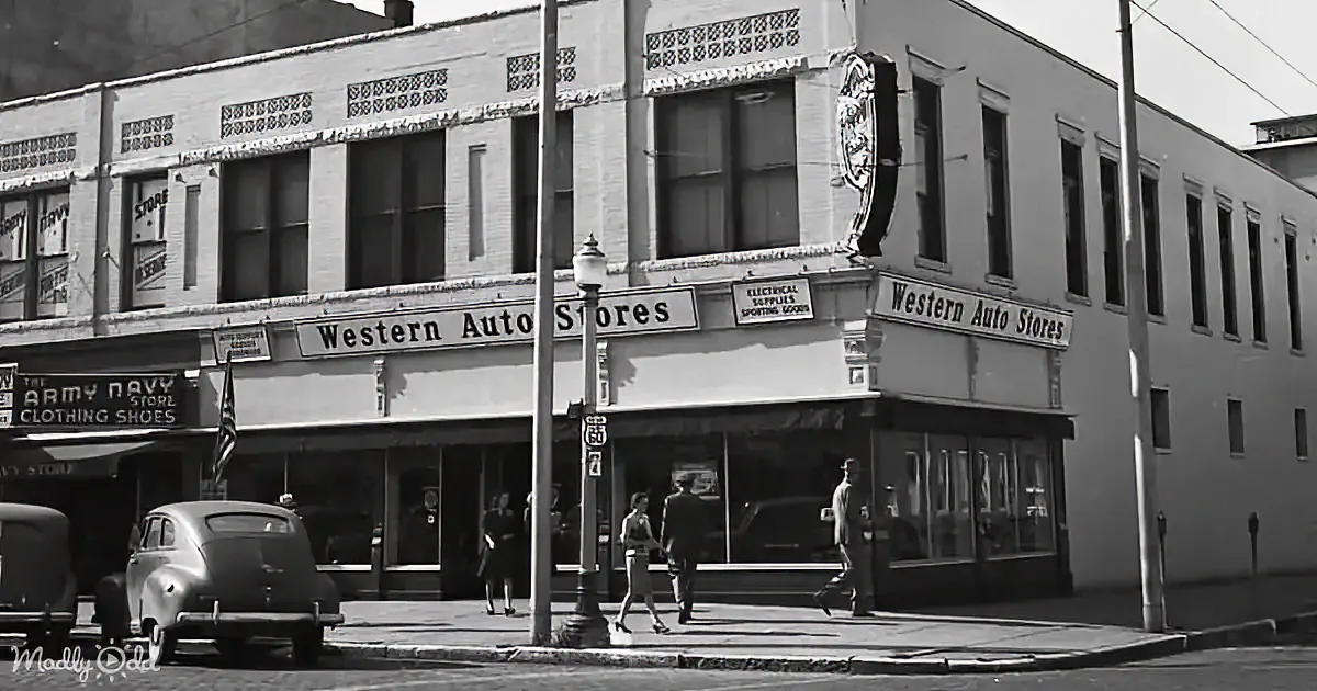Western Auto Stores building corner, vintage cars, pedestrians, signboards, street lamp, American flag.