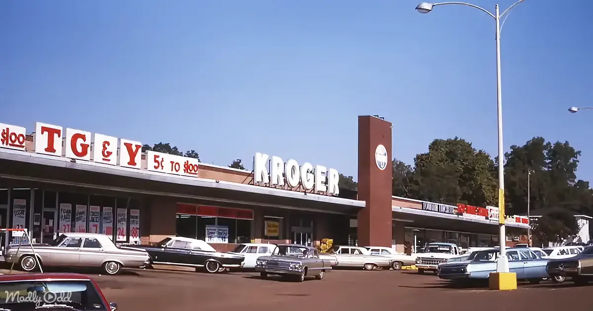 A Kroger grocery store with vintage cars parked in front under a clear blue sky.