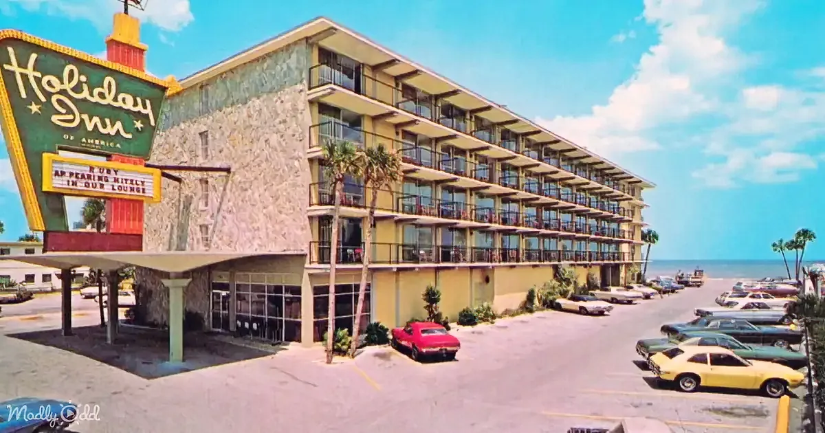 Holiday Inn sign with retro cars, palm trees, and a multi-story hotel building by the beach.