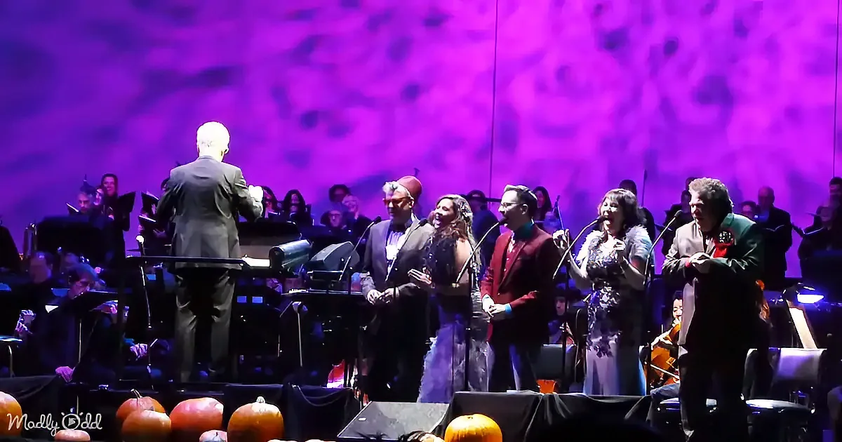 Conductor leads a festive ensemble with pumpkins and a vibrant purple backdrop.