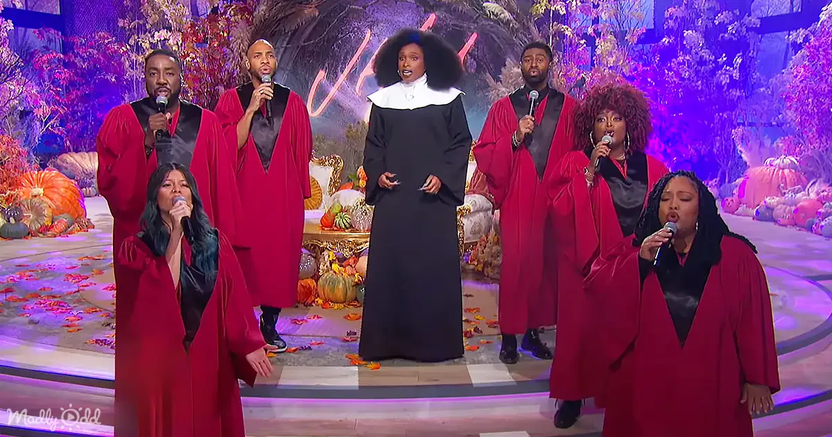 A group of singers in red robes perform on stage with a backdrop of autumn leaves and pumpkins.