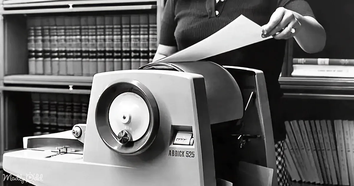 A person operates a vintage document scanner labeled "ABDICK 525" in a library setting.