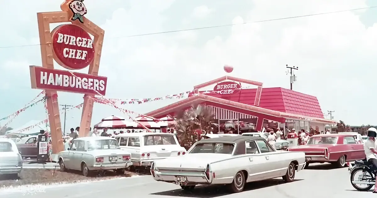 A Burger Chef restaurant with vintage cars and people in a drive-in setting.