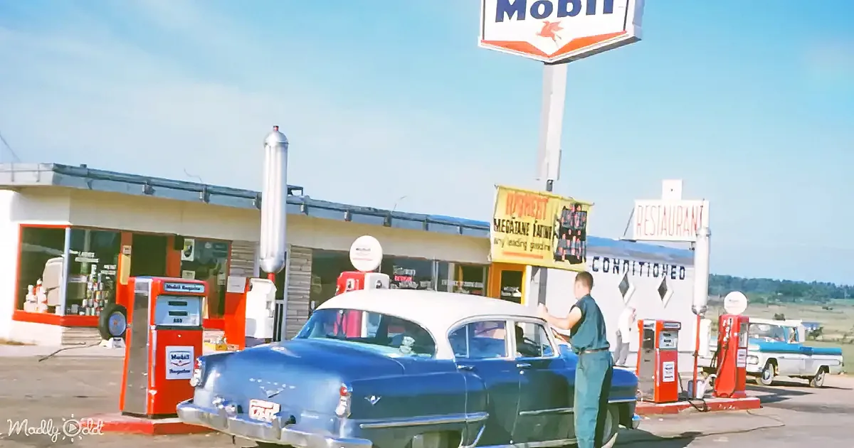 A vintage Mobil gas station with a blue car being serviced, red pumps, and a clear blue sky.