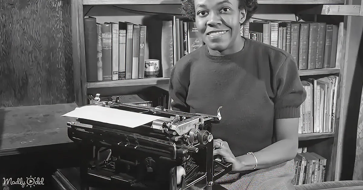 A woman smiles while typing on a vintage typewriter in a room filled with books.
