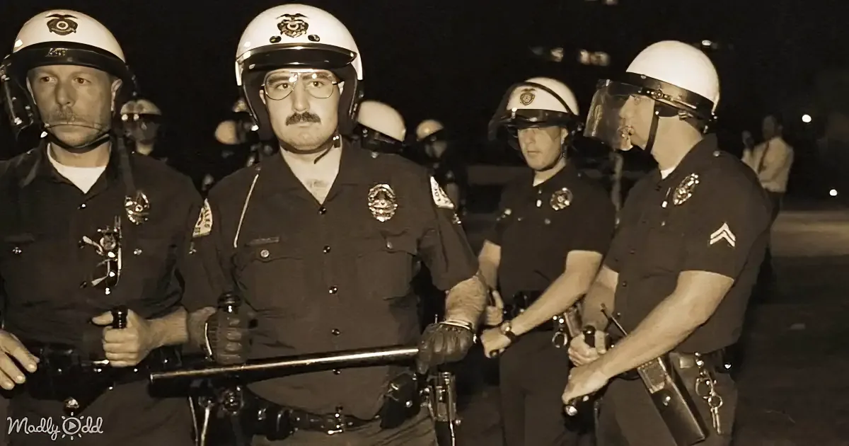Police officers in helmets and uniforms stand together, holding batons, in a nighttime setting.