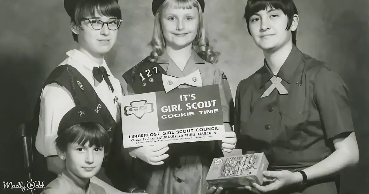 Girl Scouts hold a cookie sale sign and boxes, promoting their council's fundraising event.