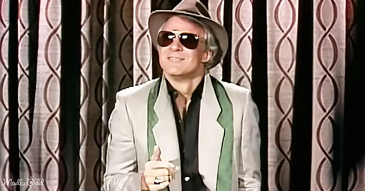 A man in a white suit and fedora holds a drink, smiling, with a patterned curtain behind him.