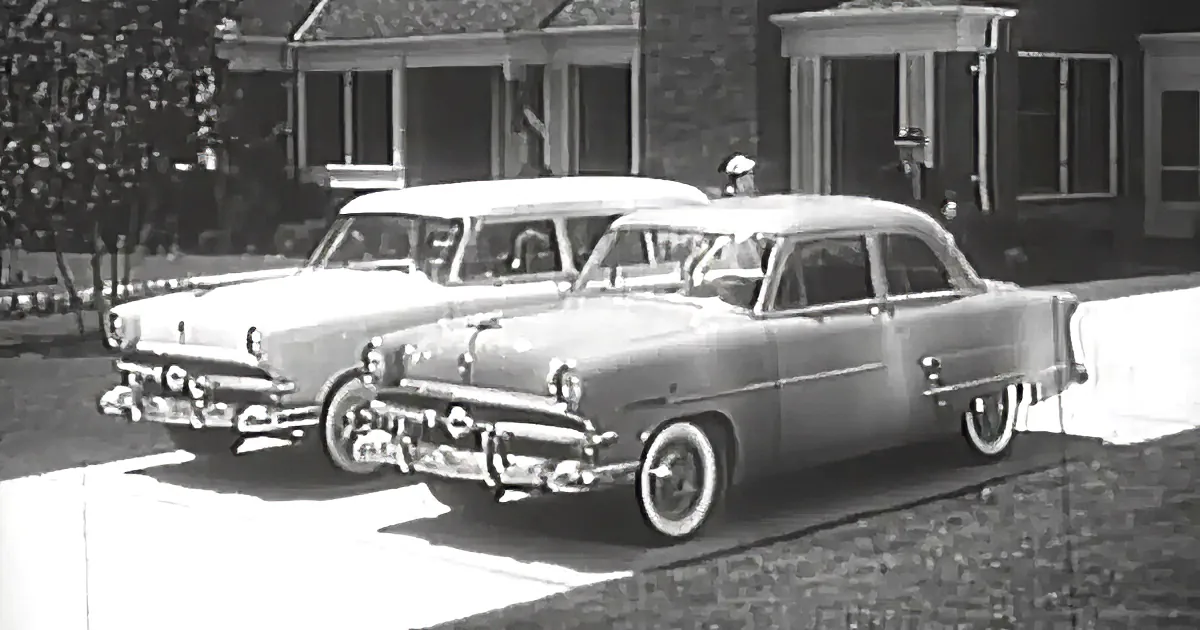 Two vintage cars parked in front of a house with a brick facade and a porch.