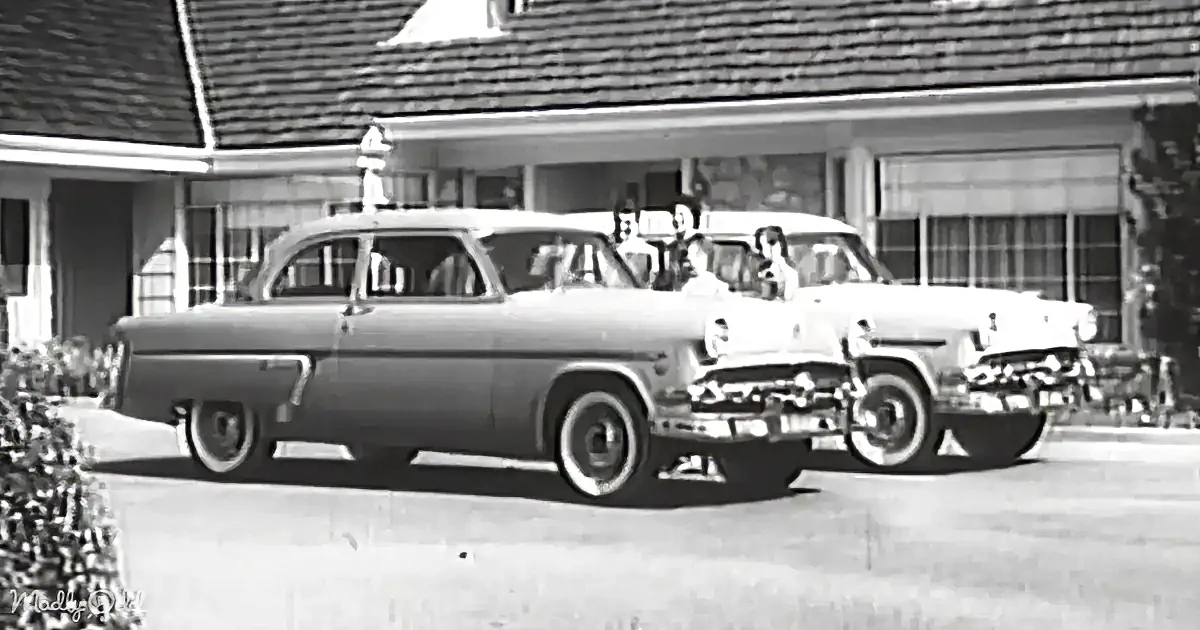 Two vintage cars parked in front of a house with people standing nearby.