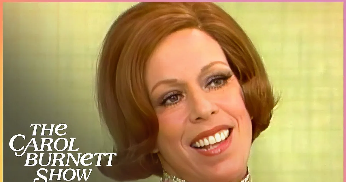 A woman with short brown hair, wearing a pink dress with a gold beaded collar, looks to the side with a surprised expression.