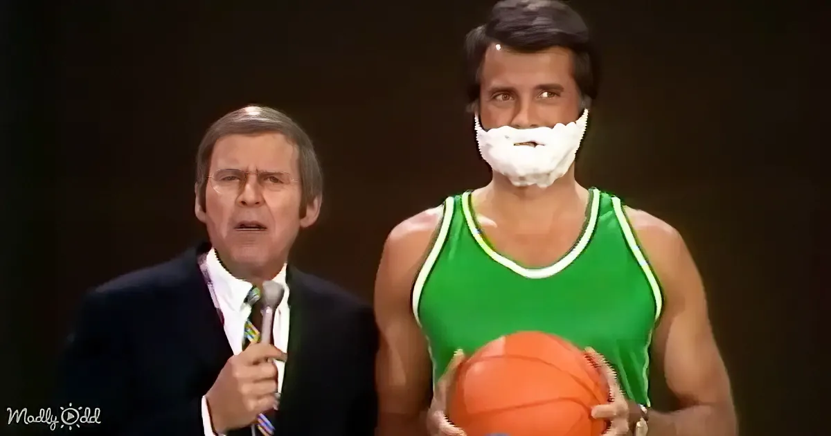 A man in a green jersey holds a basketball, another man in a suit speaks into a microphone.
