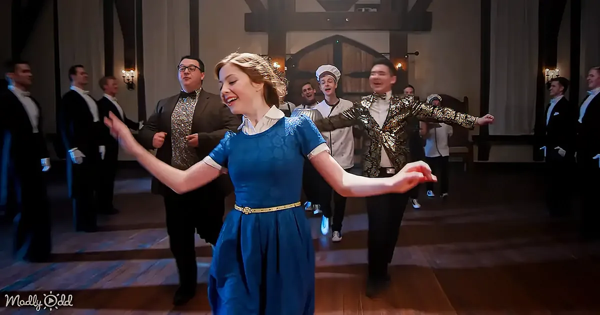 A woman in a blue dress dances joyfully in a grand hall with a group of men in formal attire.
